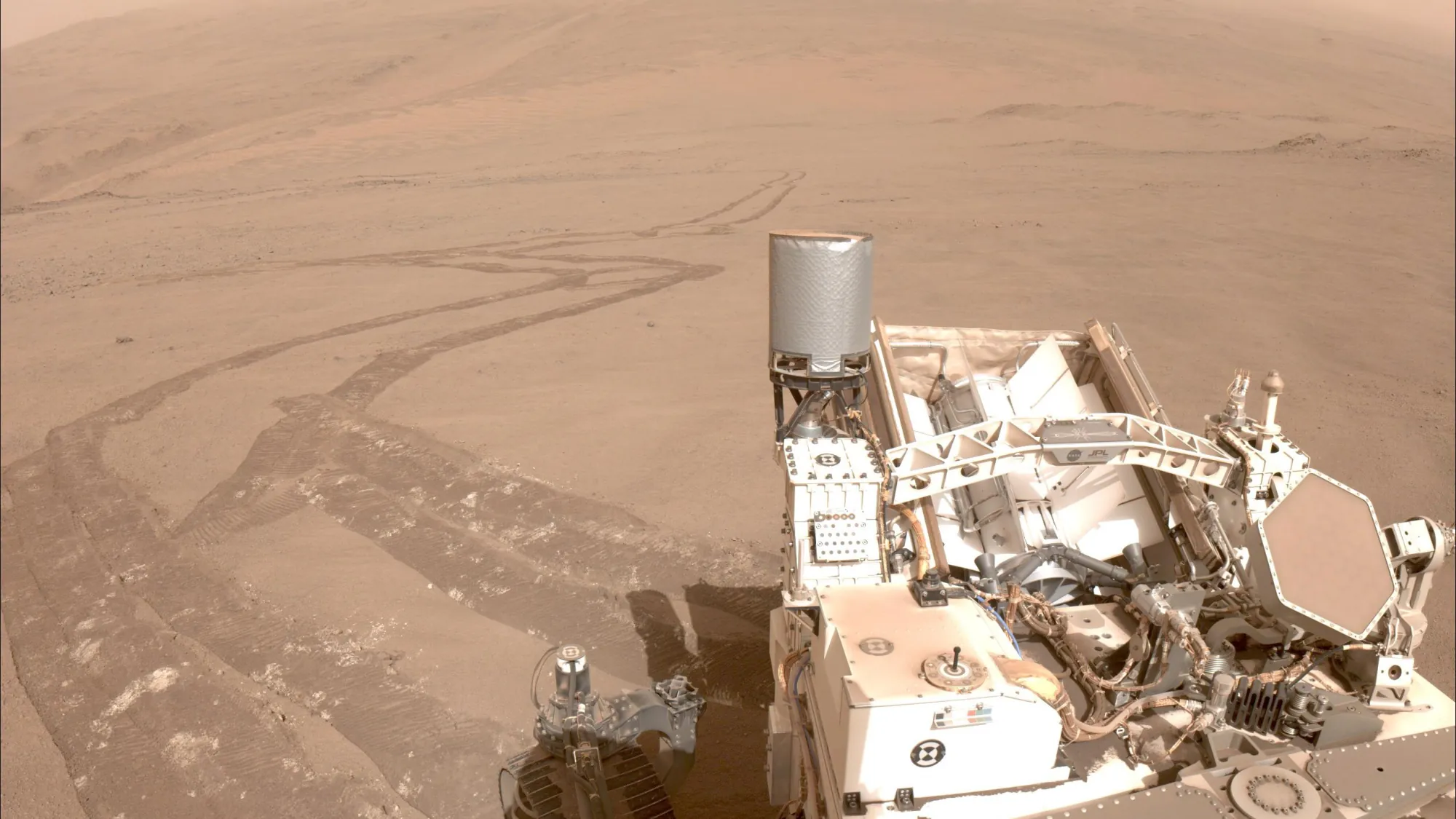Wheel tracks left by a Mars rover climbing a dusty slope, with part of the rover in view
