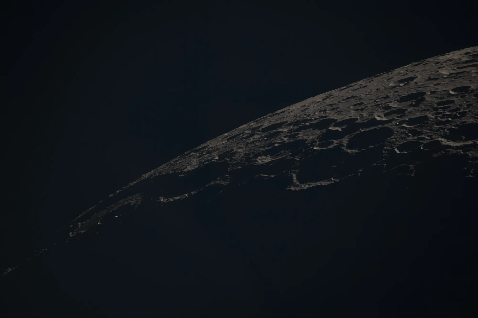 The curved edge of the Moon with craters lit at a low angle and long shadows