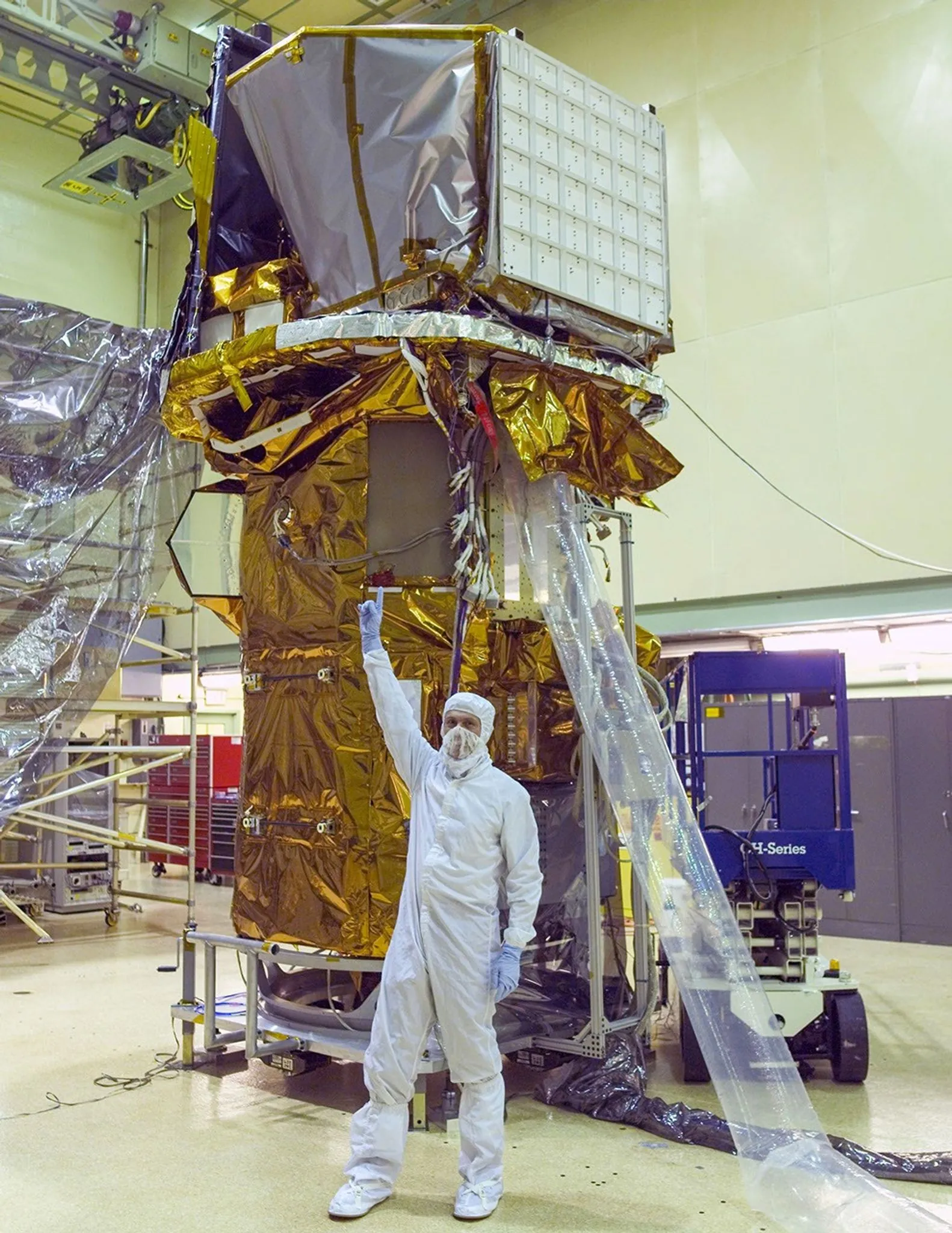 A person in a clean-room suit points up at the instruments of the Swift spacecraft, wrapped in gold foil, in a clean room